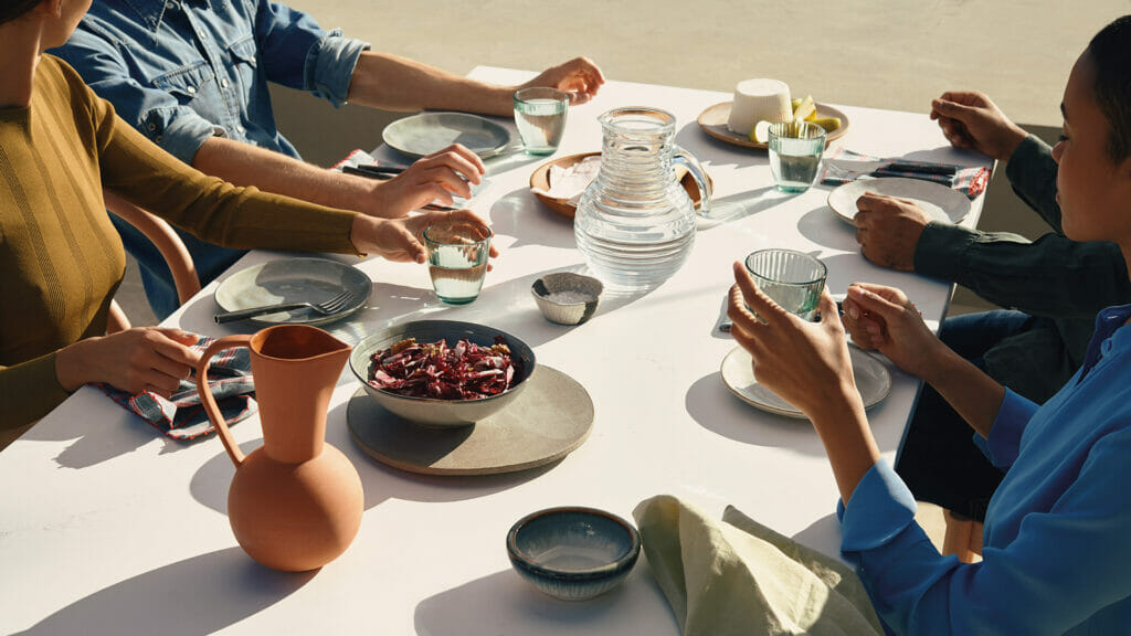 A stylish table setting with people sharing a meal, featuring dishes, drinks, and earthy decor.