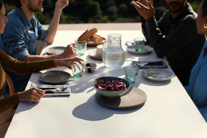 Outdoor dining scene with friends enjoying a meal at a table with plates and drinks, emphasizing a social atmosphere.