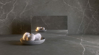 Honed dark grey surface with warm brown accents, showcasing a bowl of towels reflecting in a sleek mirror.