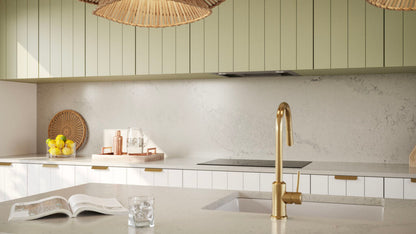 Modern kitchen featuring light green cabinetry, gold faucet, and elegant decor, with a soft grey countertop.