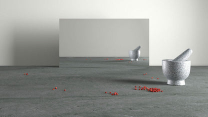 Minimalist scene with a mortar and pestle on a textured gray surface, reflecting in a mirror, with scattered red pepper berries.