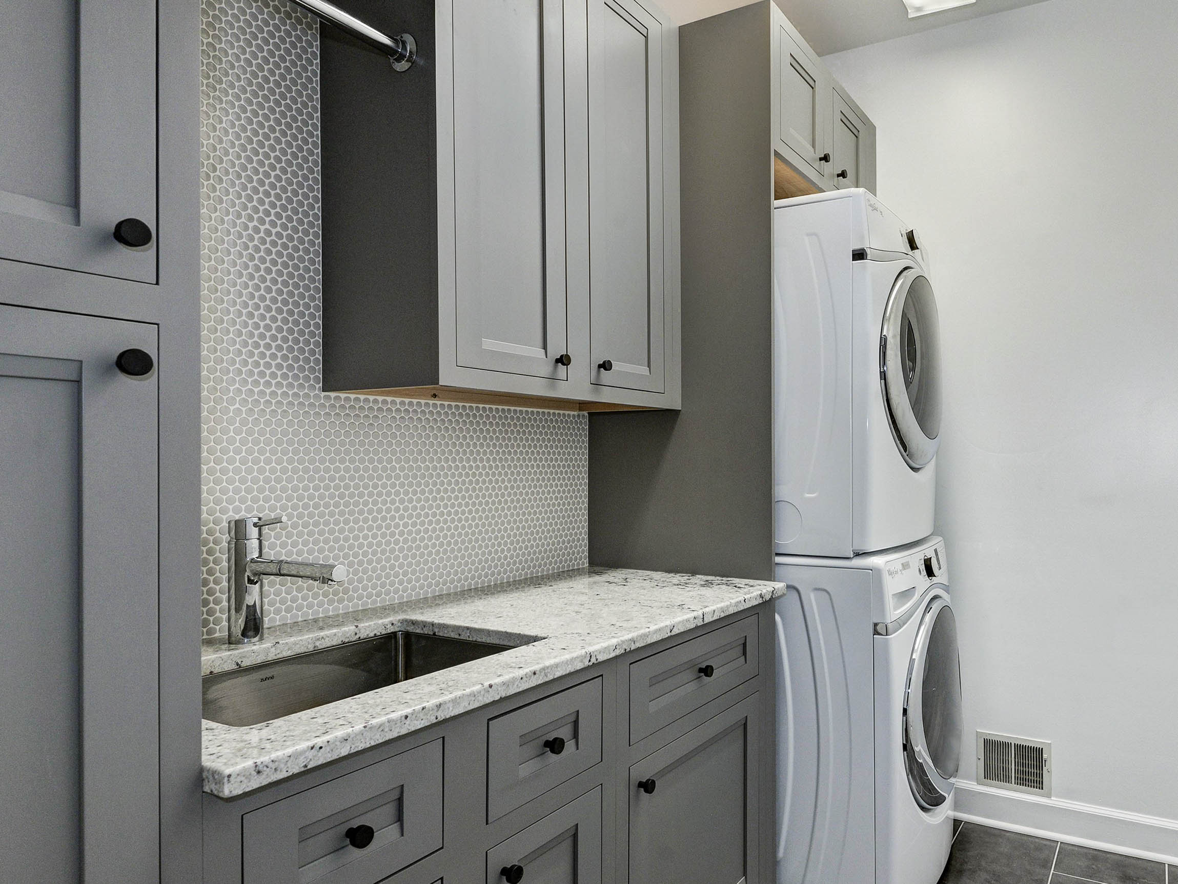 Modern laundry room featuring Shiloh gray cabinets, granite countertops, and stacked washer-dryer setup.