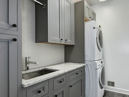 Modern laundry room featuring Shiloh gray cabinets, granite countertops, and stacked washer-dryer setup.