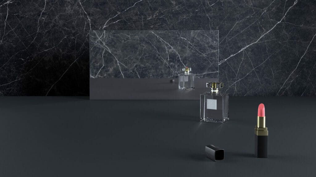 Perfume bottle and pink lipstick on a sleek dark marble countertop with a reflective mirror.